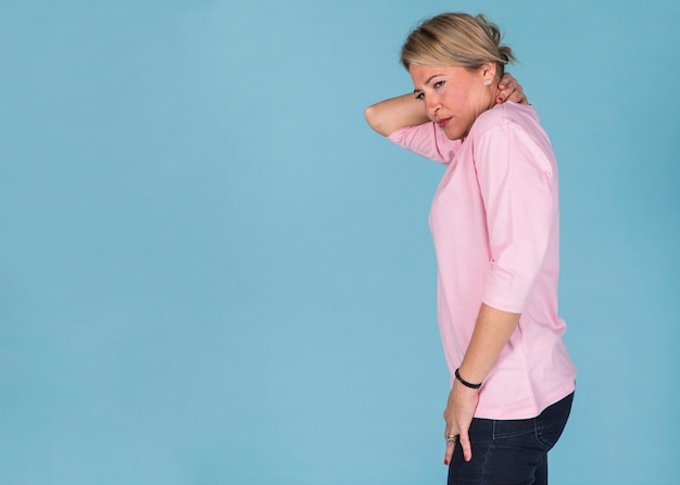 Kostenloses Foto seitenansicht einer frau, die unter nackenschmerzen gegen blaue tapete leidet