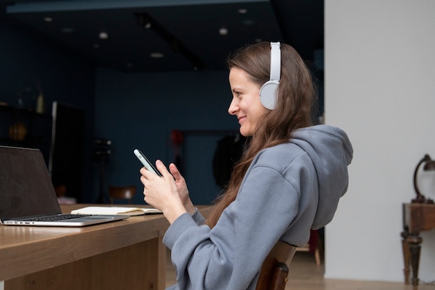 Seitenansicht einer Frau, die von zu Hause aus mit Smartphone und Kopfhörern arbeitet