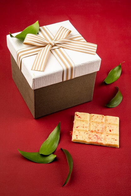 Seitenansicht einer Geschenkbox gebunden mit Schleife und weißer Tafel Schokolade auf rotem Tisch