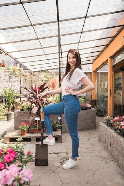 Seitenansicht einer glücklichen Frau mit der Schaufel, die im Gewächshaus steht