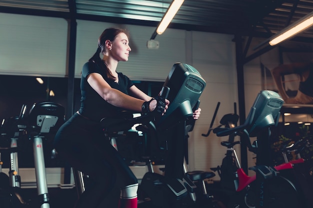 Seitenansicht einer jungen frau, die auf hometrainer in der turnhalle fährt