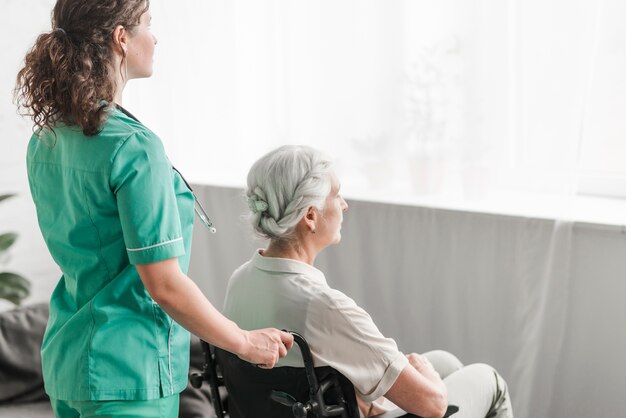 Seitenansicht einer Krankenschwester, die arbeitsunfähigen Patienten auf Rollstuhl drückt