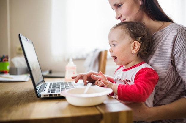 Seitenansicht einer Mutter mit ihrem Baby, das Laptop verwendet