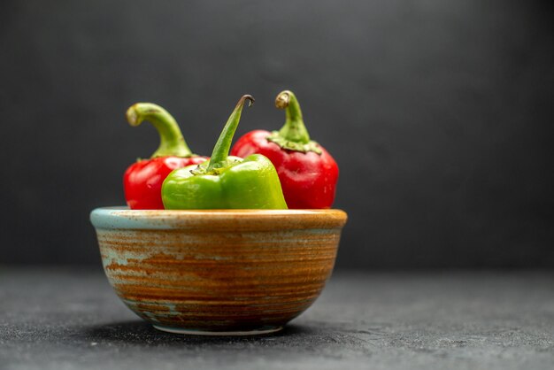 Seitenansicht einer Schüssel mit Paprika in der Mitte auf dunkelgrauem Tisch mit dunkelgrünem Hintergrund