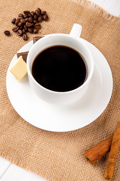 Seitenansicht einer Tasse Kaffee mit Zimtstangen und Kaffeebohnen verstreut auf rustikalem Hintergrund