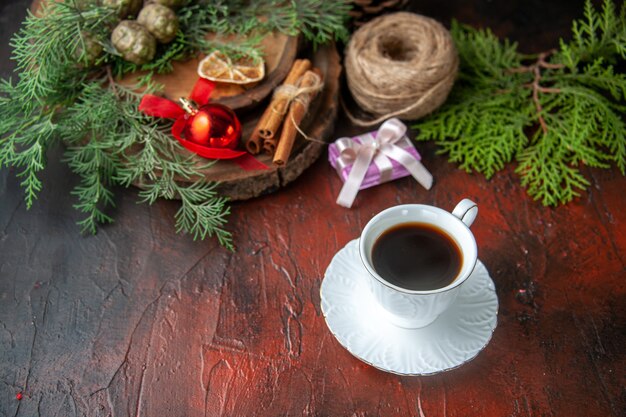 Seitenansicht einer Tasse Schwarztee-Tannenzweige und geschlossenem Spiralnotizbuch mit Stift-Zimt-Limonen-Kugel aus Seil auf dunklem Hintergrund