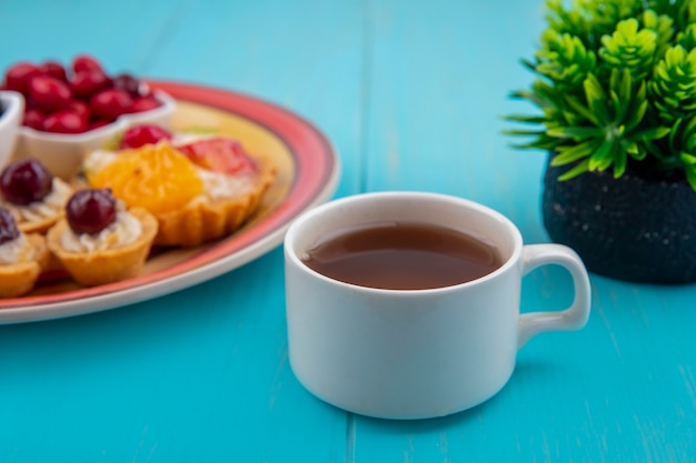 Seitenansicht einer Tasse Tee mit einem Teller Törtchen auf einem blauen hölzernen Hintergrund