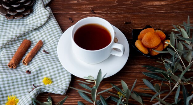 Seitenansicht einer Tasse Tee mit getrockneten Aprikosen und Zimtstangen auf Holz