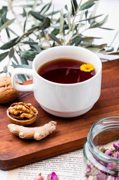 Seitenansicht einer Tasse Tee mit Ingwer und Walnüssen auf Holzbrett