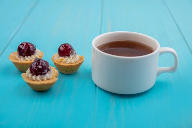 Seitenansicht einer Tasse Tee mit Mini-Traubentörtchen lokalisiert auf einem blauen hölzernen Hintergrund