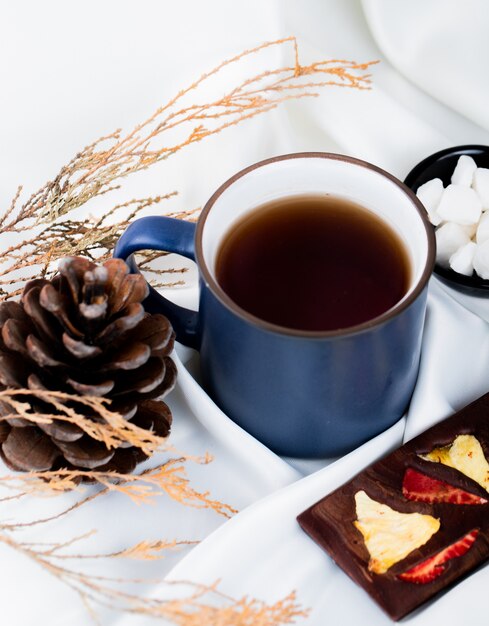 Seitenansicht einer Tasse Tee mit Schokoriegel und Tannenzapfen auf Weiß