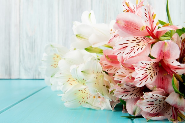 Seitenansicht eines Blumenstraußes der Alstroemeria-Blumen der rosa und weißen Farbe auf blauem hölzernem Hintergrund