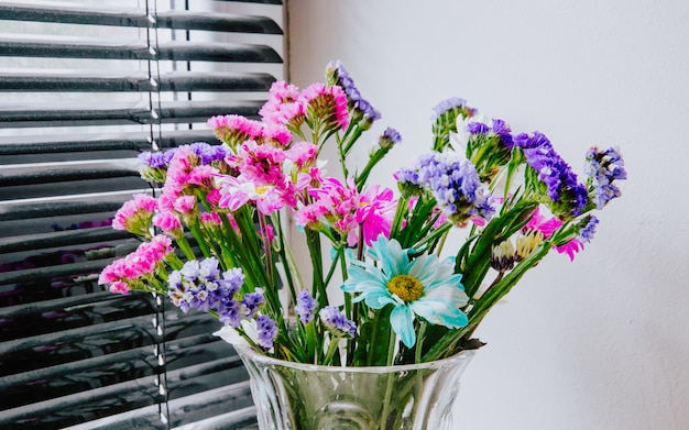 Kostenloses Foto seitenansicht eines blumenstraußes der rosa weißen lila und blauen farbstatice und der chrysanthemenblumen in einer glasvase am weißen wandhintergrund