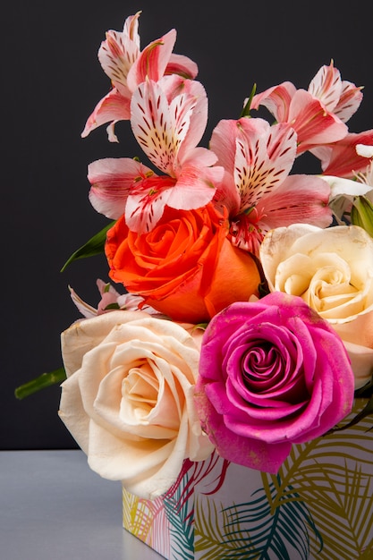 Seitenansicht eines Blumenstraußes von bunten Rosen und rosa Farbe Alstroemeria Blumen in einer Geschenkbox auf schwarzem Tisch