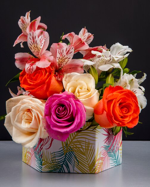 Seitenansicht eines Blumenstraußes von bunten Rosen und rosa Farbe Alstroemeria Blumen in einer Geschenkbox auf schwarzem Tisch