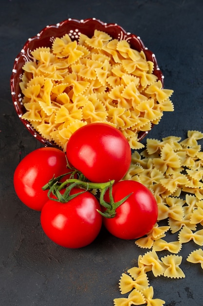 Seitenansicht eines Bündels frischer Tomaten mit rohen Nudelfarfalle, die auf Schwarz verstreut sind