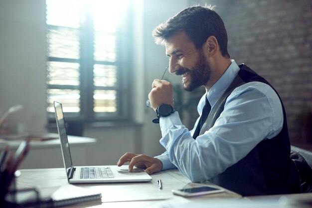 Seitenansicht eines glücklichen Geschäftsmannes, der während der Arbeit im Büro einen Computer benutzt