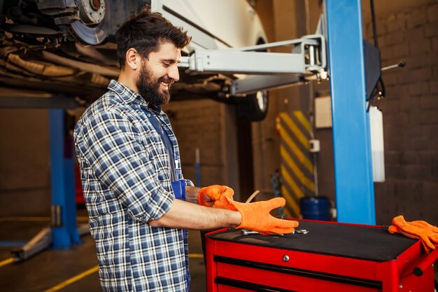 Seitenansicht eines Handwerkers, der Handschuhe für eine Arbeit mit einem Auto in einer Tankstelle anzieht