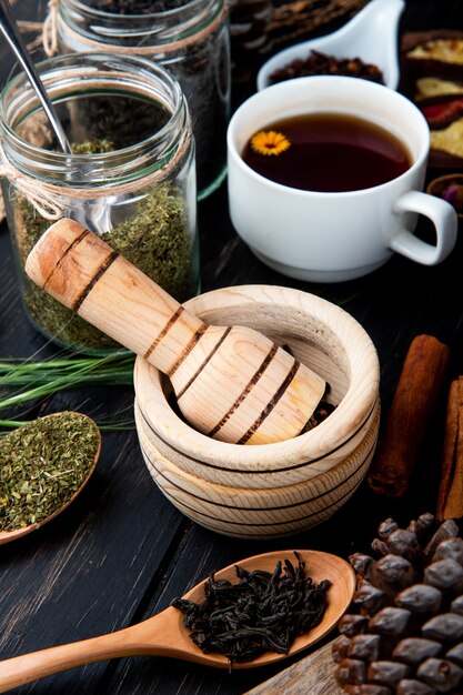 Seitenansicht eines Holzmörsers mit schwarzen Pfefferkörnern und einer Tasse Tee auf rustikalem