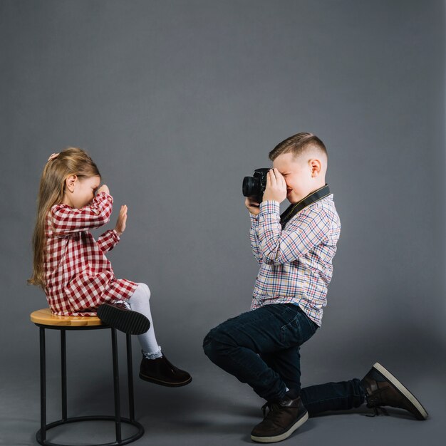 Seitenansicht eines Jungen, der Foto eines Mädchens macht, das auf Schemel mit Kamera sitzt