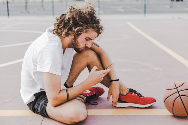 Seitenansicht eines jungen männlichen Basketball-Spielers, der Smartphone verwendet