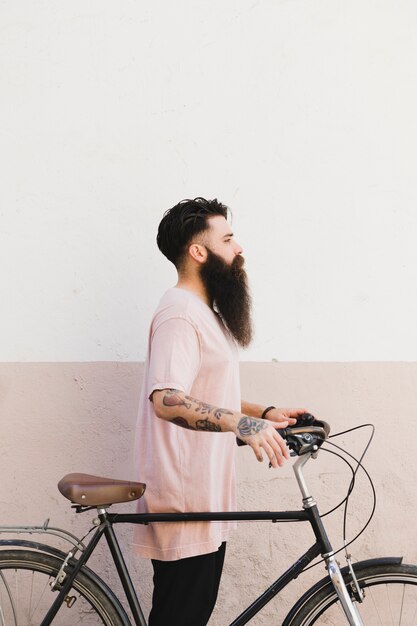 Seitenansicht eines jungen Mannes, der mit seinem Fahrrad gegen Wand steht