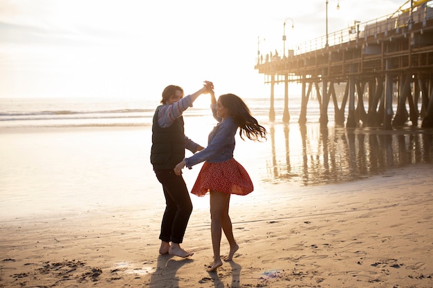 Seitenansicht eines jungen Paares, das bei Sonnenuntergang am Strand tanzt