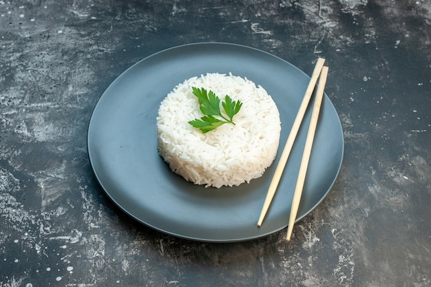 Seitenansicht eines köstlichen Reisgerichts, serviert mit Grün und Stäbchen auf einem schwarzen Teller auf dunklem Hintergrund