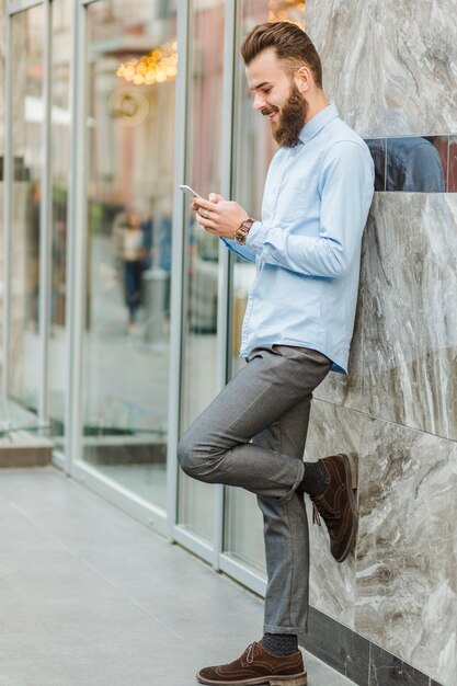 Seitenansicht eines lächelnden jungen Mannes, der Mobiltelefon verwendet