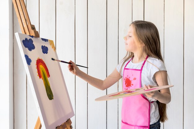 Seitenansicht eines Mädchens, das in der Hand die hölzerne Palette malt auf dem Gestell mit Malerpinsel hält
