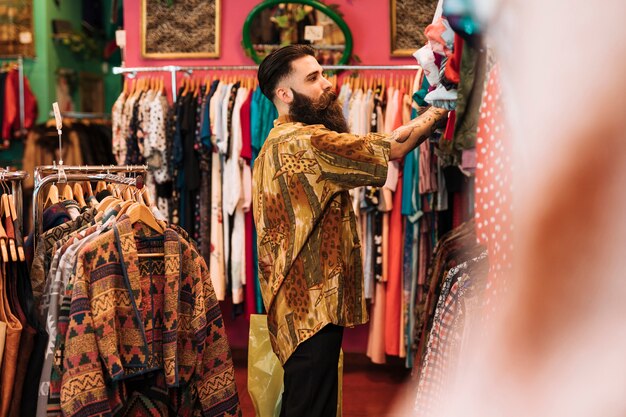 Seitenansicht eines Mannes, der die Kleidung hängt an der Schiene im Shop betrachtet