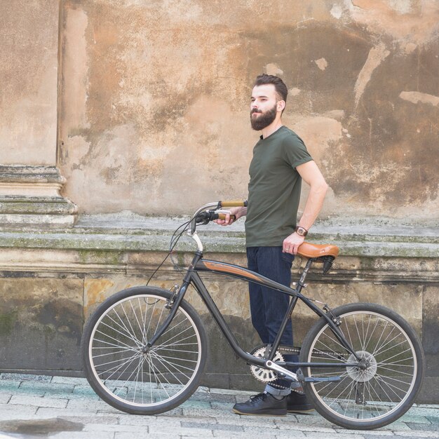 Seitenansicht eines Mannes, der mit seinem Fahrrad vor alter Wand steht