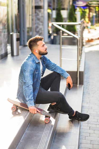 Seitenansicht eines Mannes mit dem Skateboard, das auf Treppenhaus sitzt