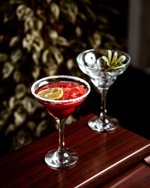 Seitenansicht eines roten Cocktails mit gehacktem Eis und einer Zitronenscheibe im Glas auf dem Tisch