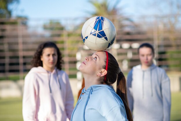 Seitenansicht eines Teenager-Mädchens, das mit Ball spielt. Sportliches Mädchen in Sportbekleidung, das Ball auf der Stirn hält, das Spielen übt und Fähigkeiten des Trainings für ihr Team zeigt. Gesunder Lebensstil, Mannschaftssportkonzept