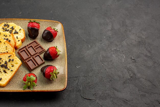 Seitenansicht Erdbeeren und Kuchenkuchen mit Schokoladenschokolade überzogene Erdbeeren auf grauem Teller auf der linken Seite des Tisches