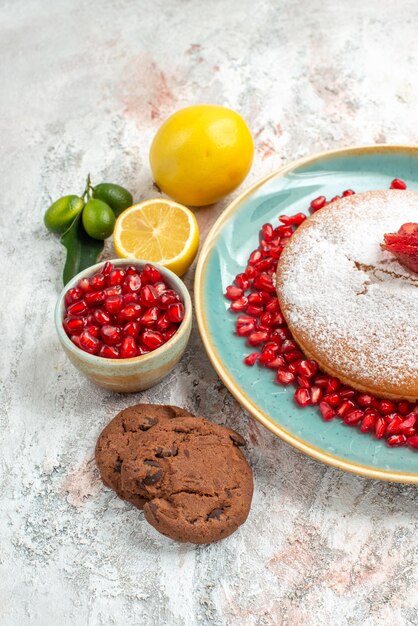 Seitenansicht Erdbeerkuchen blauer Kuchenteller mit Erdbeeren und Granatapfel neben der Zitronenschale mit Granatapfel und Keksen auf dem Teller