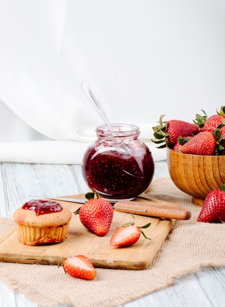 Seitenansicht Erdbeermarmelade mit Cupcake frische Erdbeere in einer Holzschale und Messer auf weißem Hintergrund