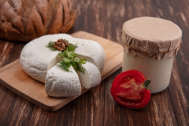 Seitenansicht-Feta-Käse auf einem Ständer mit Tomate und Joghurt in einem Glas auf einem hölzernen Hintergrund