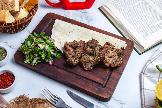 Seitenansicht Fleischbasturma-Kebab auf Fladenbrot mit Kräutern und Zwiebeln auf einem Brett
