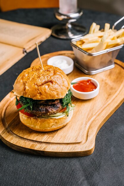 Seitenansicht Fleischburger mit Rindfleischpastetchen Tomatengrünsalat in Burgerbrötchen mit Pommes Frites Mayo und Ketchup auf einem Teller