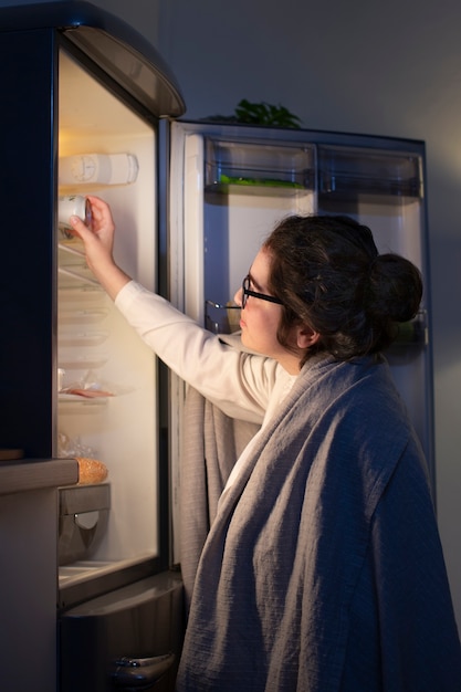 Seitenansicht Frau, die den Kühlschrank auf einen Snack überprüft