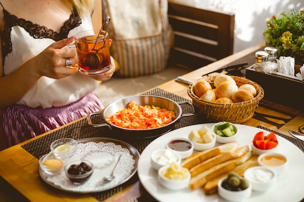 Seitenansicht Frühstücksset Eier nach aserbaidschanischer Art mit Tomaten Toast Marmelade Honig frische Tomaten Gurken Käse französische Brötchen und schwarzer Tee in einer Tasse