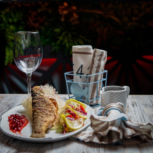 Seitenansicht gebratener Fisch mit Glas Wein und Zitrone im weißen Teller