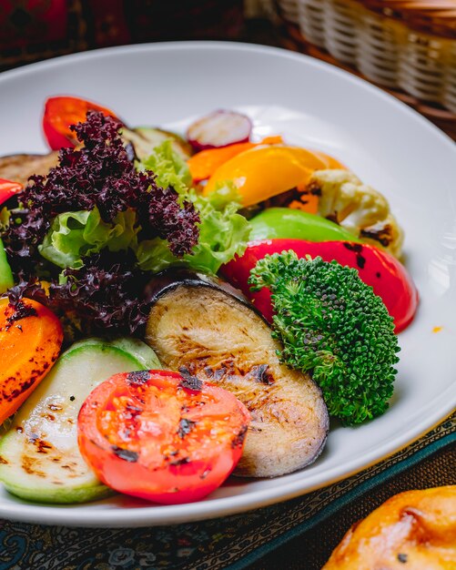 Seitenansicht gegrilltes Gemüse Auberginenkürbis Paprika Salat Tomaten Blumenkohl und Radieschen auf einem Teller