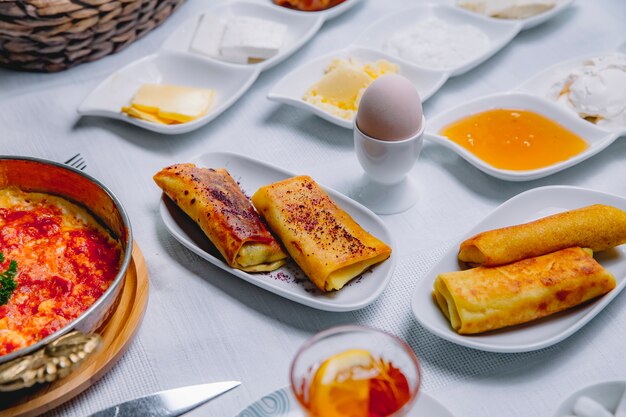 Seitenansicht gerollte Pfannkuchen mit gekochtem Ei und Honig auf dem Tisch serviert Frühstück