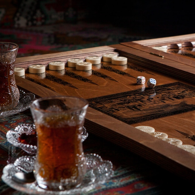 Kostenloses Foto seitenansicht glas tee mit backgammon und marmelade auf teppich tisch