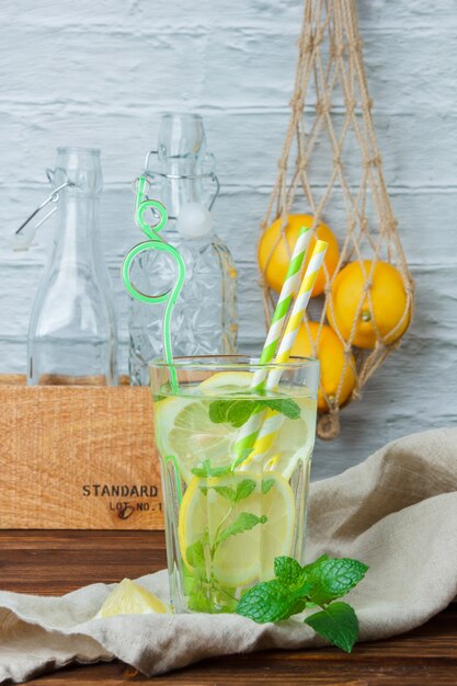 Seitenansicht Glas Zitronensaft mit Holzkiste und Zitronen auf Holz und weißer Oberfläche. vertikal