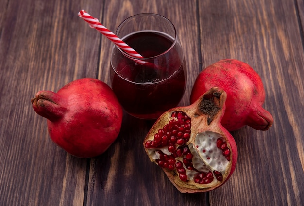 Seitenansicht Granatäpfel mit einem Glas Saft und einem roten Strohhalm auf einer Holzwand