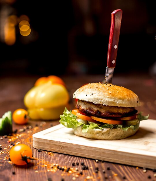 Seitenansicht-Hühnchen-Burger mit Salatblatt-Tomaten-Hühnchen-Pastetchen in Burgerbrötchen und schwarzem Pfeffer auf dem Tisch